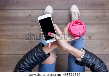 Close up of women\'s hands holding cell telephone with blank copy space screen for your advertising text message or promotional content. Young hipster girl sitting on Wooden floor and using smart phone