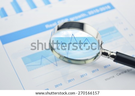 Magnifying glass over financial chart and graph business, analysis concept