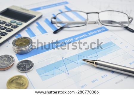 Glasses, pen, calculator and coin on financial chart and graph, accounting background