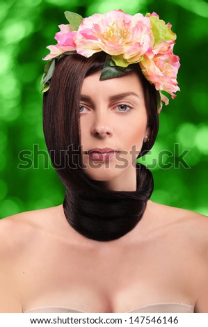 beautiful brunette girl wearing a wreath of pink tsetov with hair tied in a knot around the neck on a green background with bokeh