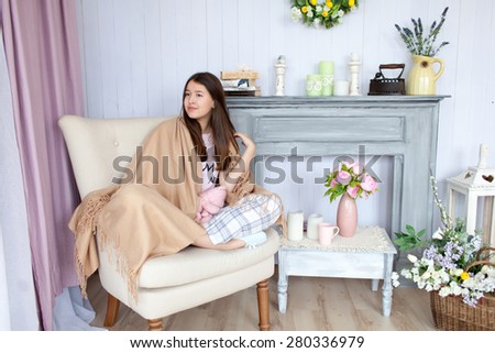 Girl in pajama with beige cover sitting in armchair.