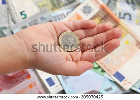 One euro coin on a children\'s hand on background of euro banknotes