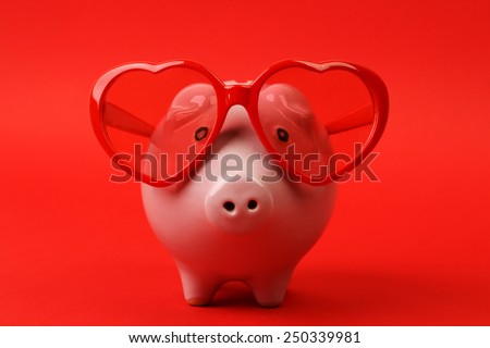 Piggy bank in love with red heart sunglasses standing on red background