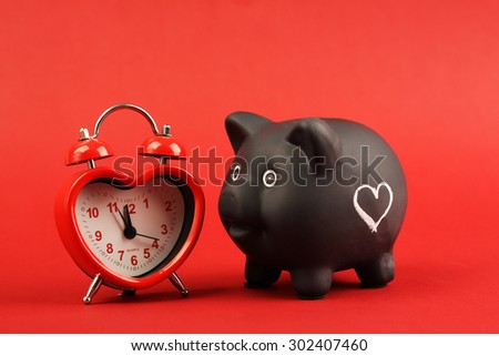 Black piggy bank with white heart and heart alarm clock on red background
