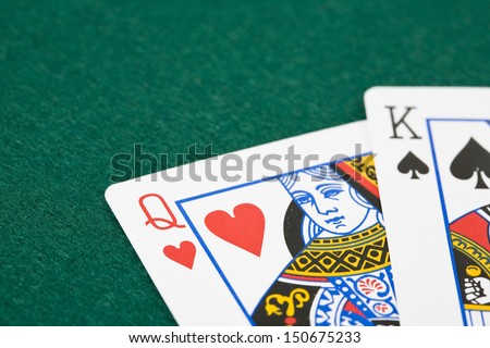 Closeup of queen of hearts and king of spades playing cards over green felt surface