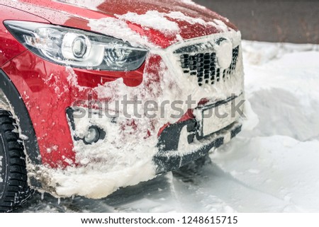 Front side of car overed with snow on a parking place.