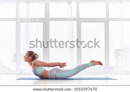 Beautiful woman practices yoga asana Salabhasana - locust pose at the yoga studio