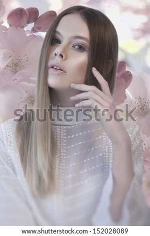Young pretty woman in white blouse with beauty long hair and hand near her face on flower background