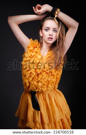 Attractive woman with hands above her head, beauty make-up, pretty long hair and yellow dress with dark belt, looking at camera
