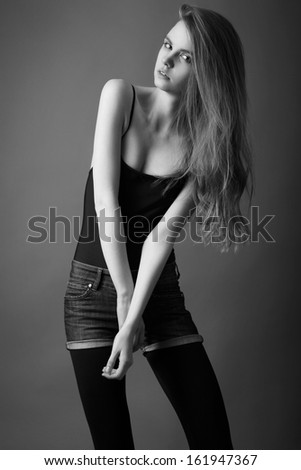 Attractive woman with pretty long hair dressed in black top, dark shorts and black leggings, looking at camera . Black and White photo