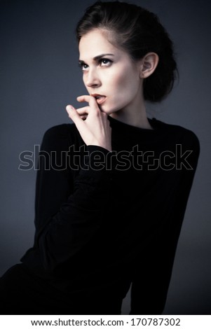 Waist up of young attractive woman with beauty hairstyle, natural make up and hand near her face, wearing black dress and looking up