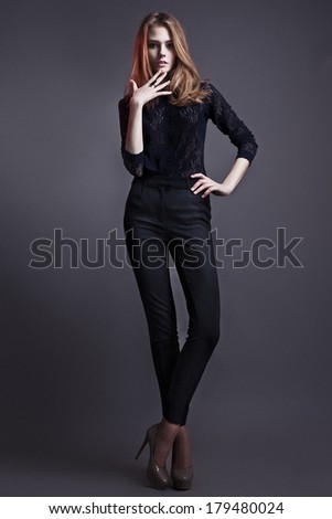 Sexy young woman with pretty long blonde hair and natural make up, dressed in black blouse and trousers, wearing high-heeled shoes, standing and looking at camera