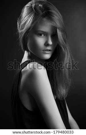 Close up profile of young female with pretty long hair and natural make-up, dressed in black dress and looking at camera. Black and White photo