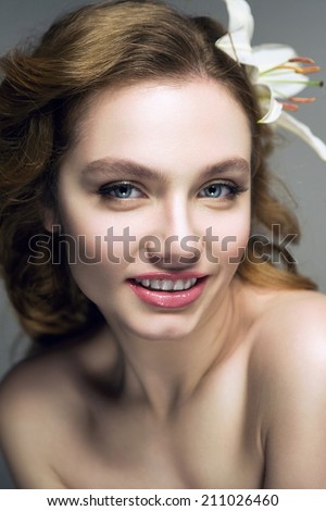 Young smiling woman with wavy hair, blue eyes, natural make up and a flower in her hair, looking at camera.