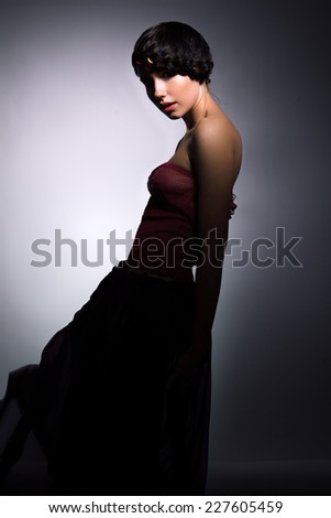 Profile of young sexy female with creative pigtail around her head, dressed in red top and dark long skirt, looking at camera
