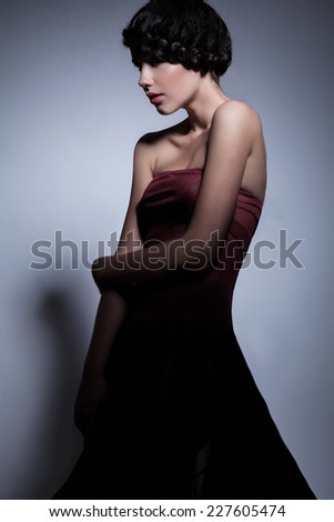 Profile of sexy female with creative pigtail around her head, dressed in red top and dark long skirt, looking away