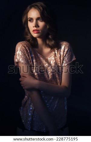 Sexy young woman with fashionable hairstyle and make-up, dressed in sparkling top and looking away