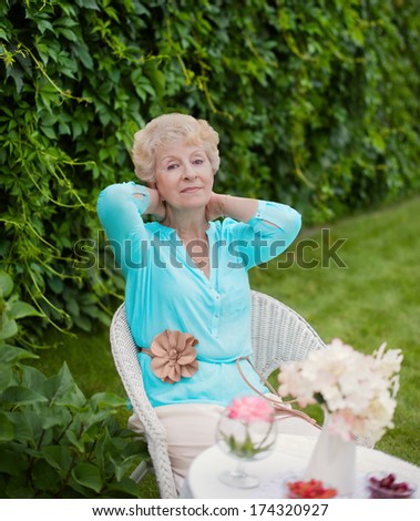 Portrait of an attractive elegant senior woman relaxing and dreaming in her home garden during a sunny day