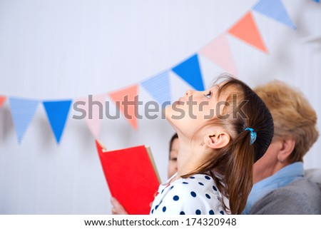 Grandmother with her little grandson and granddaughter reading book happy together at home, girl looking up