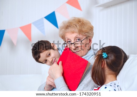 Grandmother with her little grandson and granddaughter reading book happy together at home