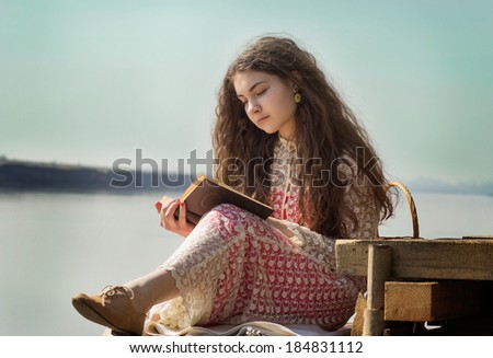 beautiful girl with long hair reads the book at the river on the mooring. retro style