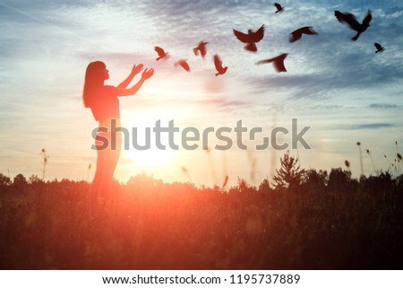 A young girl prays while enjoying nature amidst a beautiful sunset. The concept of hope, faith, religion. A flock of birds flies, a symbol of hope and freedom.