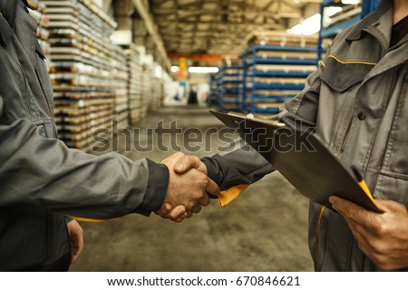Cropped close up of a worker holding clipboard shaking hands with his colleague at the industrial storage copyspace teamwork partnership metalworking hardware industry