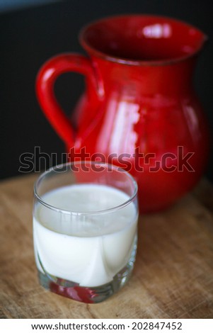 A glass of kefir/milk with a red pitcher on the background
