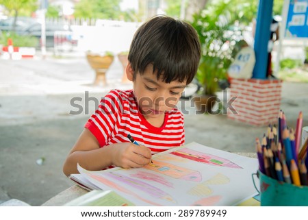 Little boy drawing picture on table outdoor;