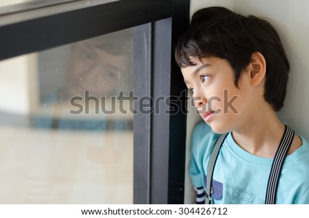 Little boy standing behind the window with sad face