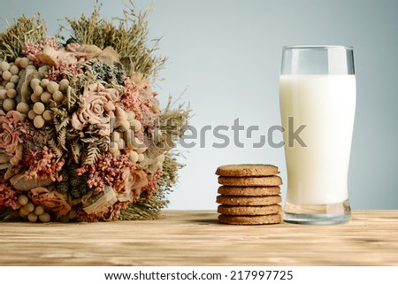 Glass of milk and cookies on vintage wooden background with dried flower bouquet