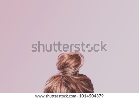 A view of the back of a woman\'s head. Hair wrapped in a bun on a light pink pastel background. Content completion concept.