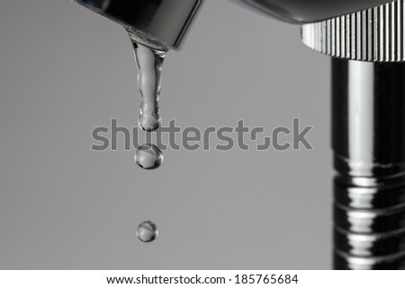 Bathroom tap leaking water drops on grey background