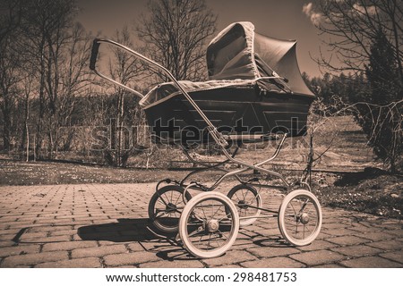 Retro style stroller baby carriage outdoors in nature on sunny day with black and white faded filter applied