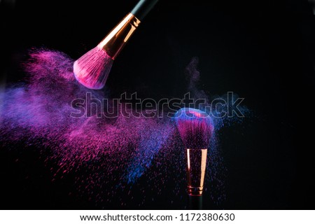 Make-up brush with colorful powder splashes explosion on black background