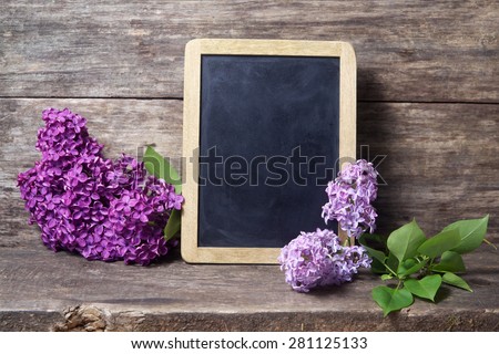 Still life with lilac flowers in a vase and blackboard on wooden background