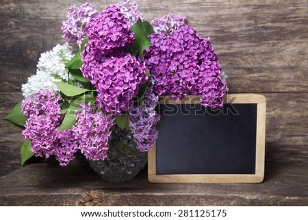 Still life with lilac flowers in a vase and blackboard on wooden background