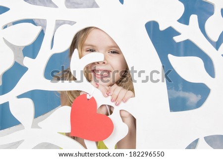 blond pretty girl smiling and looking over an ornamental tree with a card in the shape of a heart