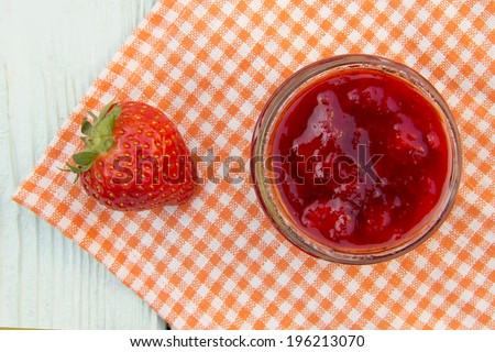 Red fresh strawberry jam in the bank stands on a wooden surface, close to the strawberries