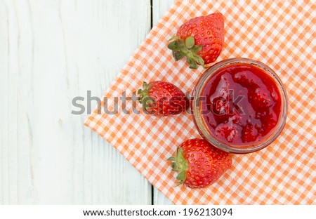 Red fresh strawberry jam in the bank stands on a wooden surface, close to the strawberries