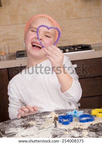 girl looking through a cookie cooking mold of the heart and smiling