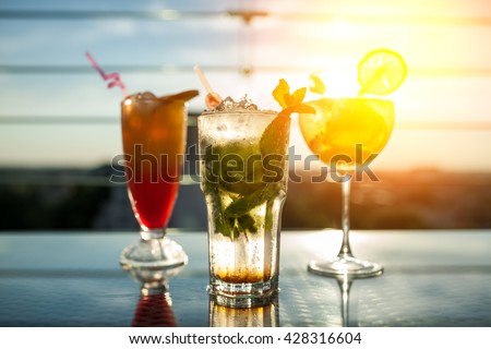 three exotic cocktails in rays of sun; fresh summer cold alcohol drinks;