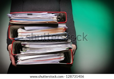 woman in grey holding stack of folders. Pile with old documents and bills on green background