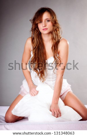 portrait of young woman long curly hair with pillow in bed gray background