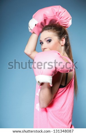 Female boxer model wearing big fun pink gloves playing sports boxing studio shot, blue background