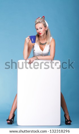 full lenght Beautiful young woman with pin-up make-up and hairstyle posing in studio with white board cup of tea