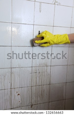 gloved hand cleaning dirty old tiles with brush in a bathroom