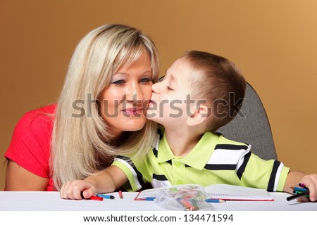 mother and son drawing together, helping with homework, child kissing mom on cheek, orange background