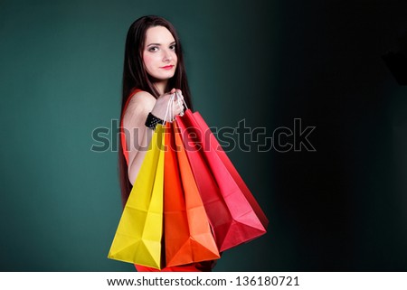 young woman long hair with paper multi coloured shopping bags on green background. Sales and discounts concept.
