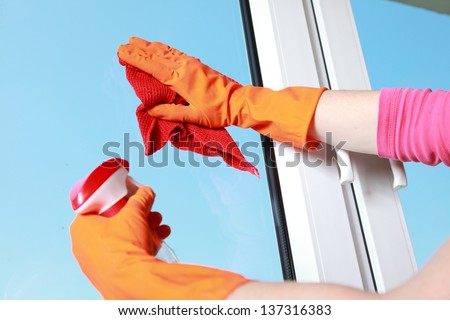 hand in orange glove cleaning window with red rag and spray detergent. Spring cleaning concept